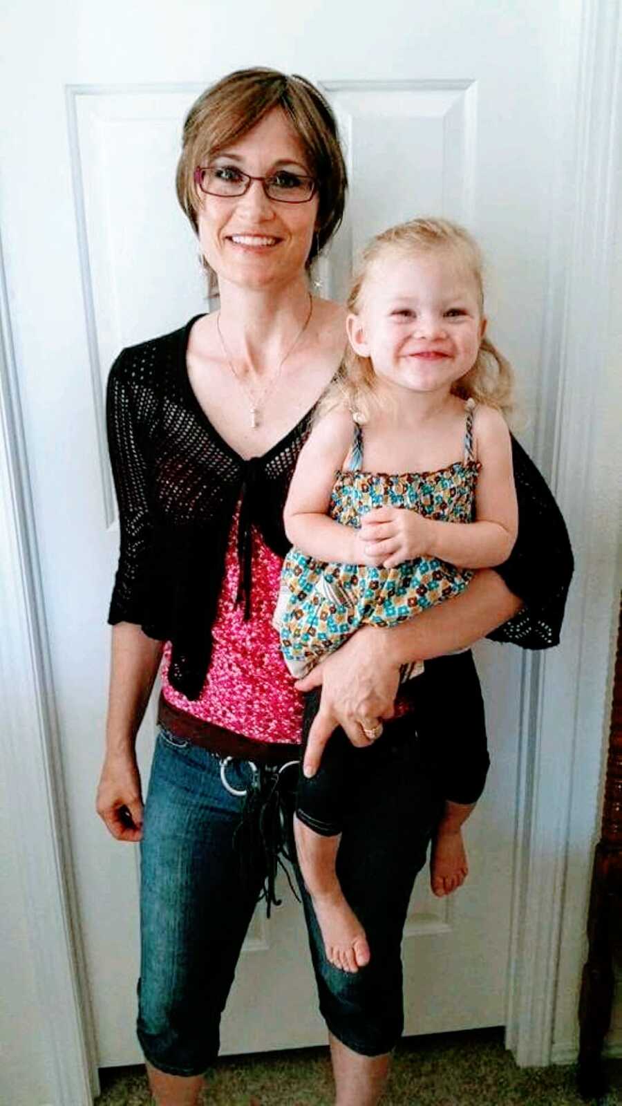 Mom of 4 holds her young daughter as they both grin at the camera