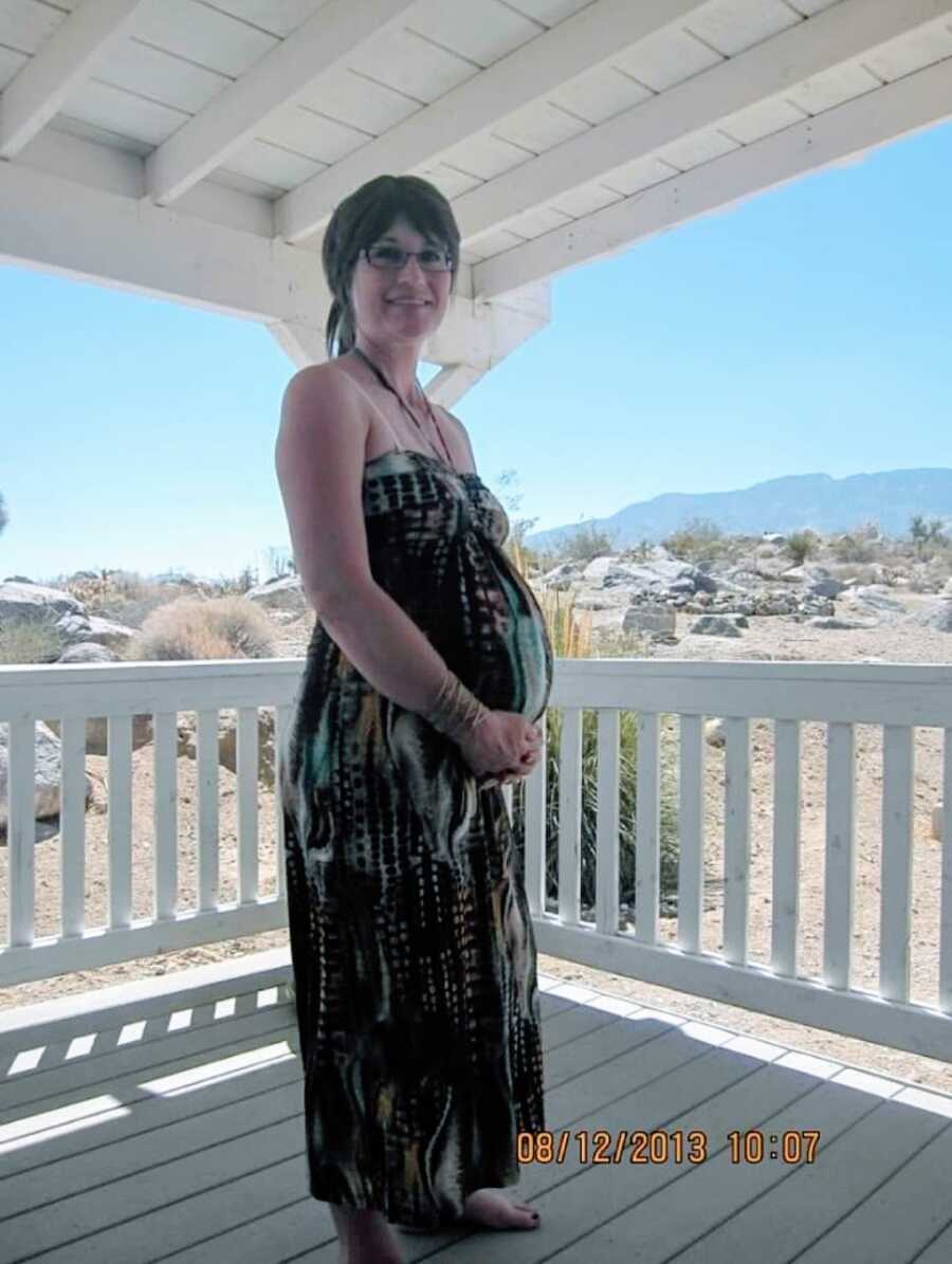 Expecting mother smiles big while showing off her pregnancy bump in a sundress