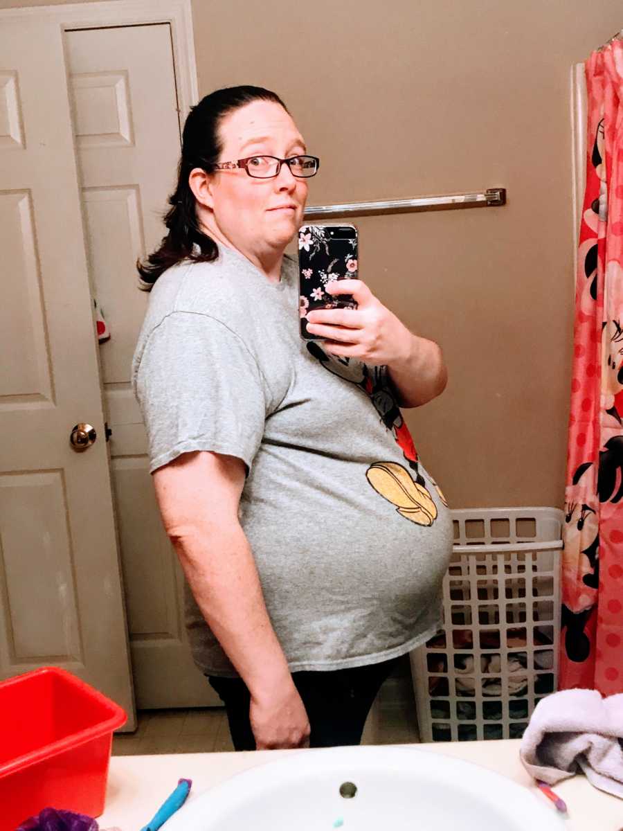 Woman pregnant with twins takes a photo of her growing belly bump in the bathroom mirror with a Mickey Mouse shirt on