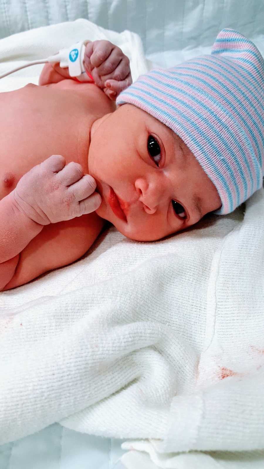 Mom takes photo of her newborn daughter, her rainbow baby, in a pink and blue striped beanie