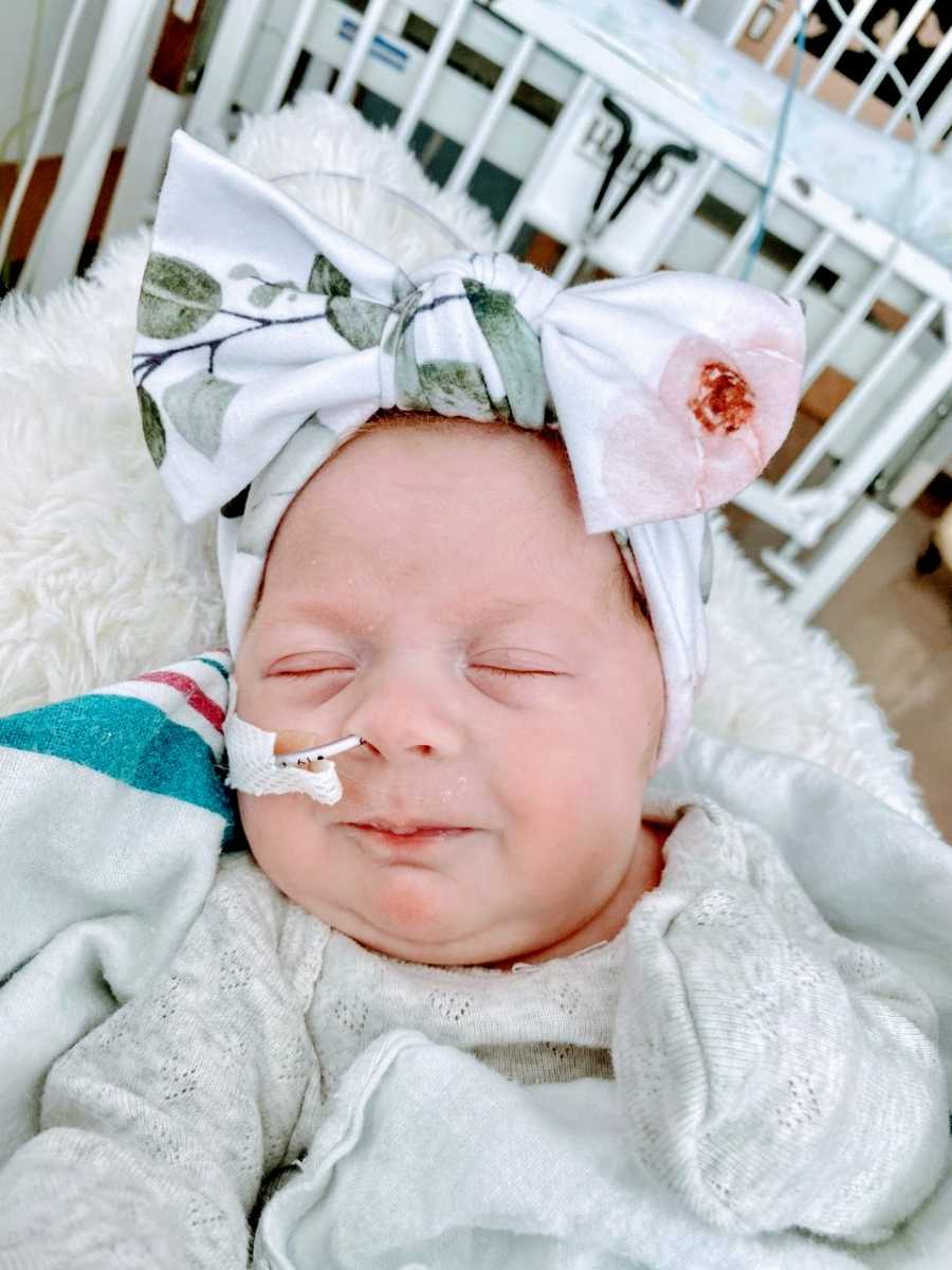 Young mom snaps photo of her rainbow baby and NICU warrior smiling in her sleep with a floral bow on her head