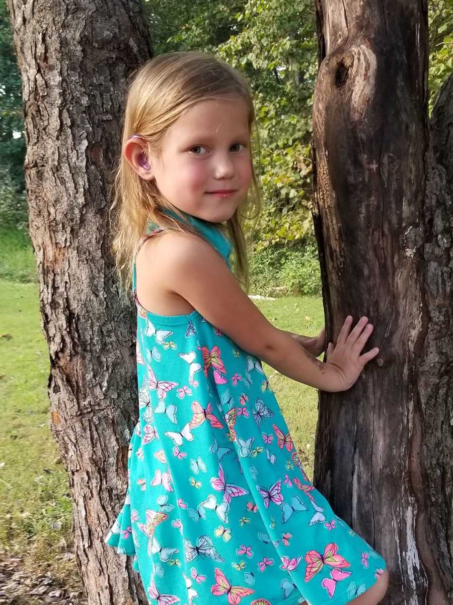 young girl holding onto a tree with hearing aids