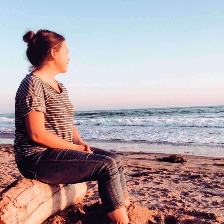 Young independent woman takes a photo watching the sunset on the beach while sitting on a log