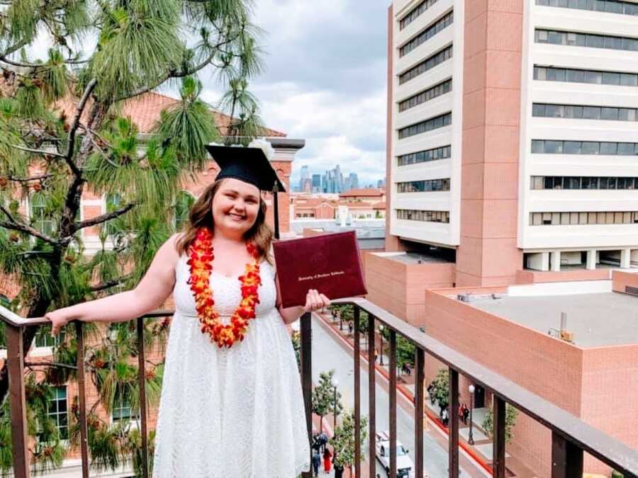 Young college student graduating from University of Southern California magna cum laude smiles with her diploma and graduation cap on