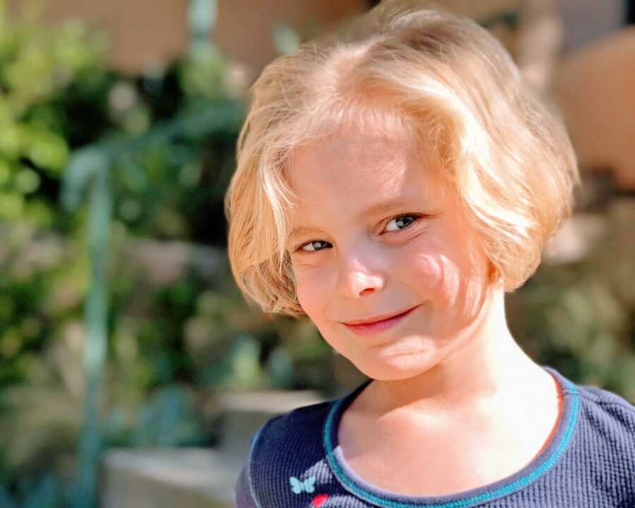 Little girl with a blonde bob smiles for a photo in a blue shirt with butterflies
