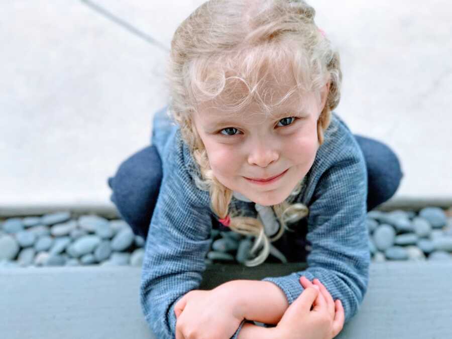 Little girl with blonde hair and blue eyes squats over a pile of rocks