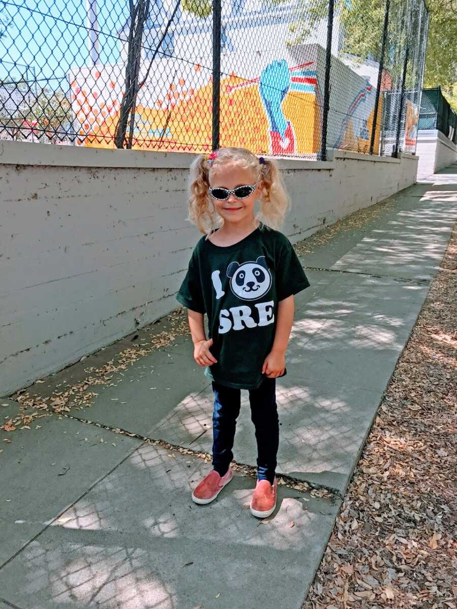 Little girl smiles for a photo while on a walk wearing a panda shirt and sunglasses