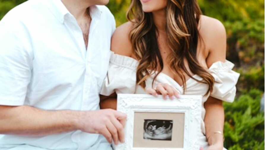 Couple in all white outfit holding up framed ultrasound picture