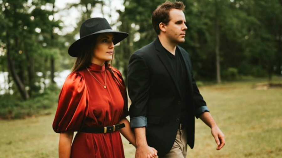 Woman in red dress and black hat holding hands with man in black blazer