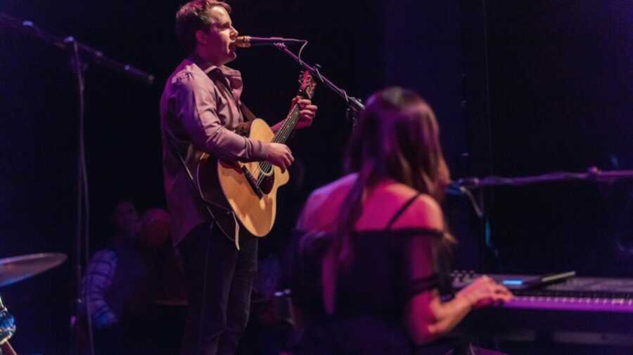 Woman singing and playing piano while man is singing and playing the guitar