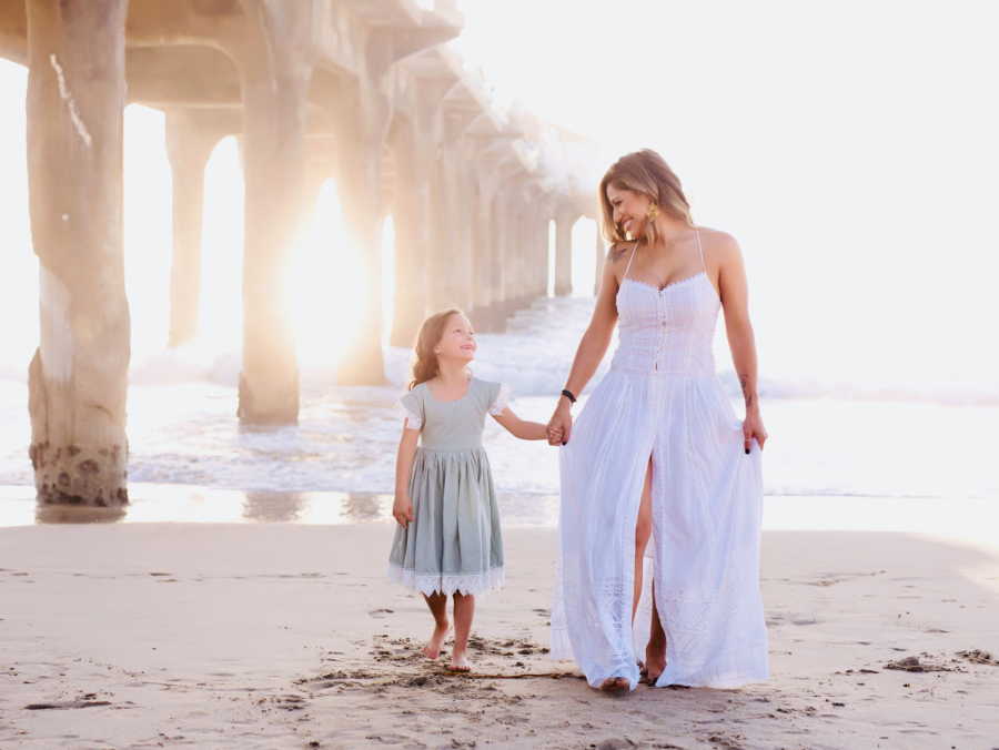 Young widow walks on the beach in a white dress with her daughter she fought so hard to have