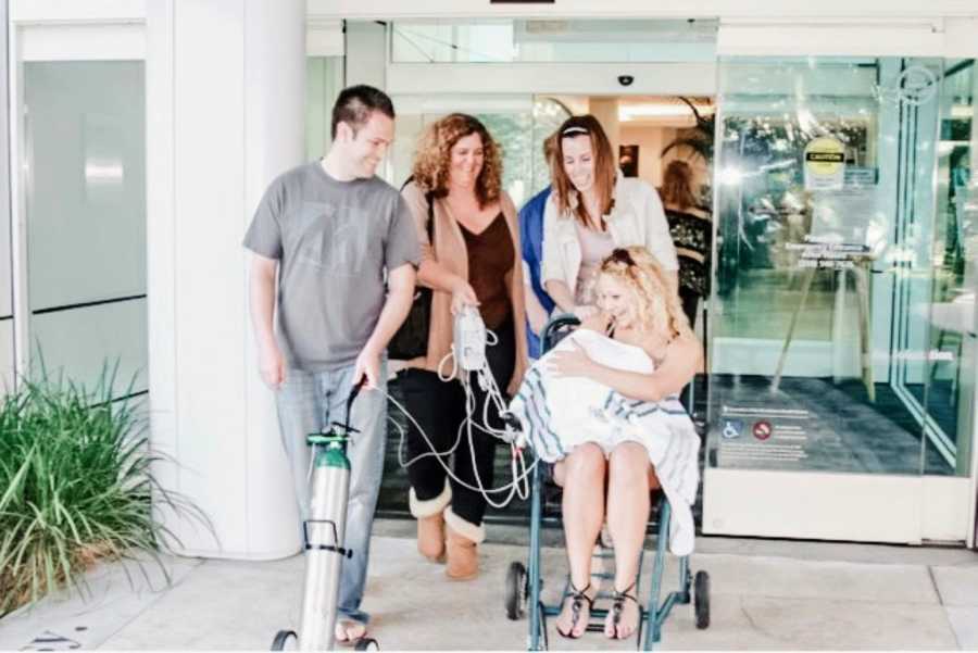 New mom gets wheeled out of the hospital with her newborn baby attached to an oxygen tank