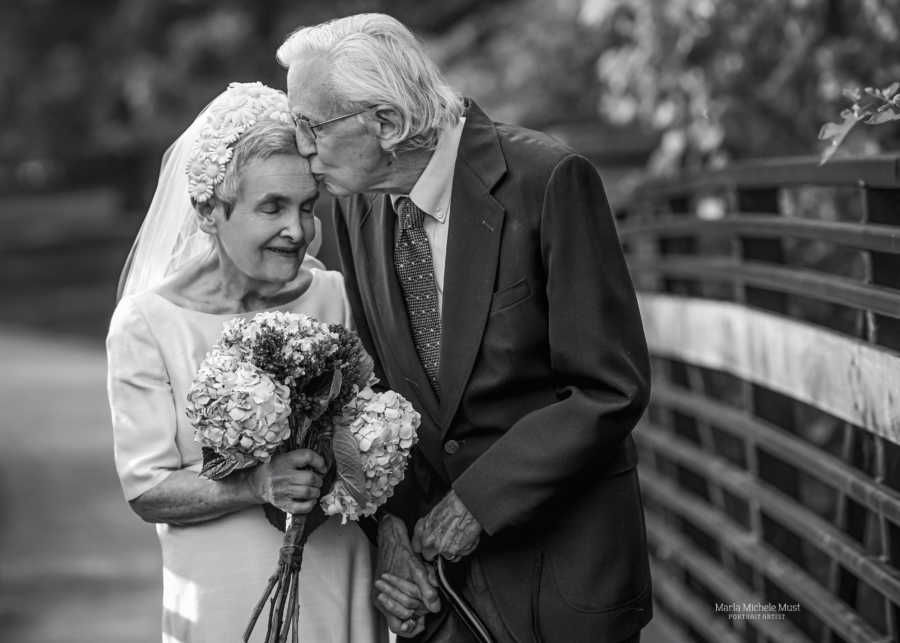 Elderly couple walk hand-in-hand while the husband kisses his wife on the forehead