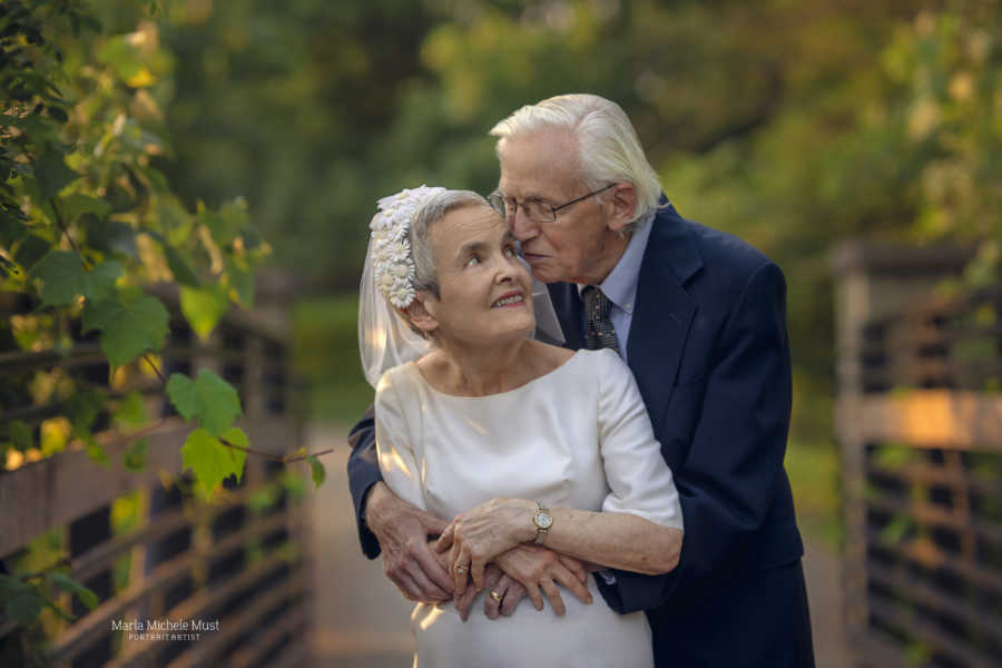 Elderly couple celebrating their 50th wedding anniversary wear their original wedding outfits and share an intimate hug