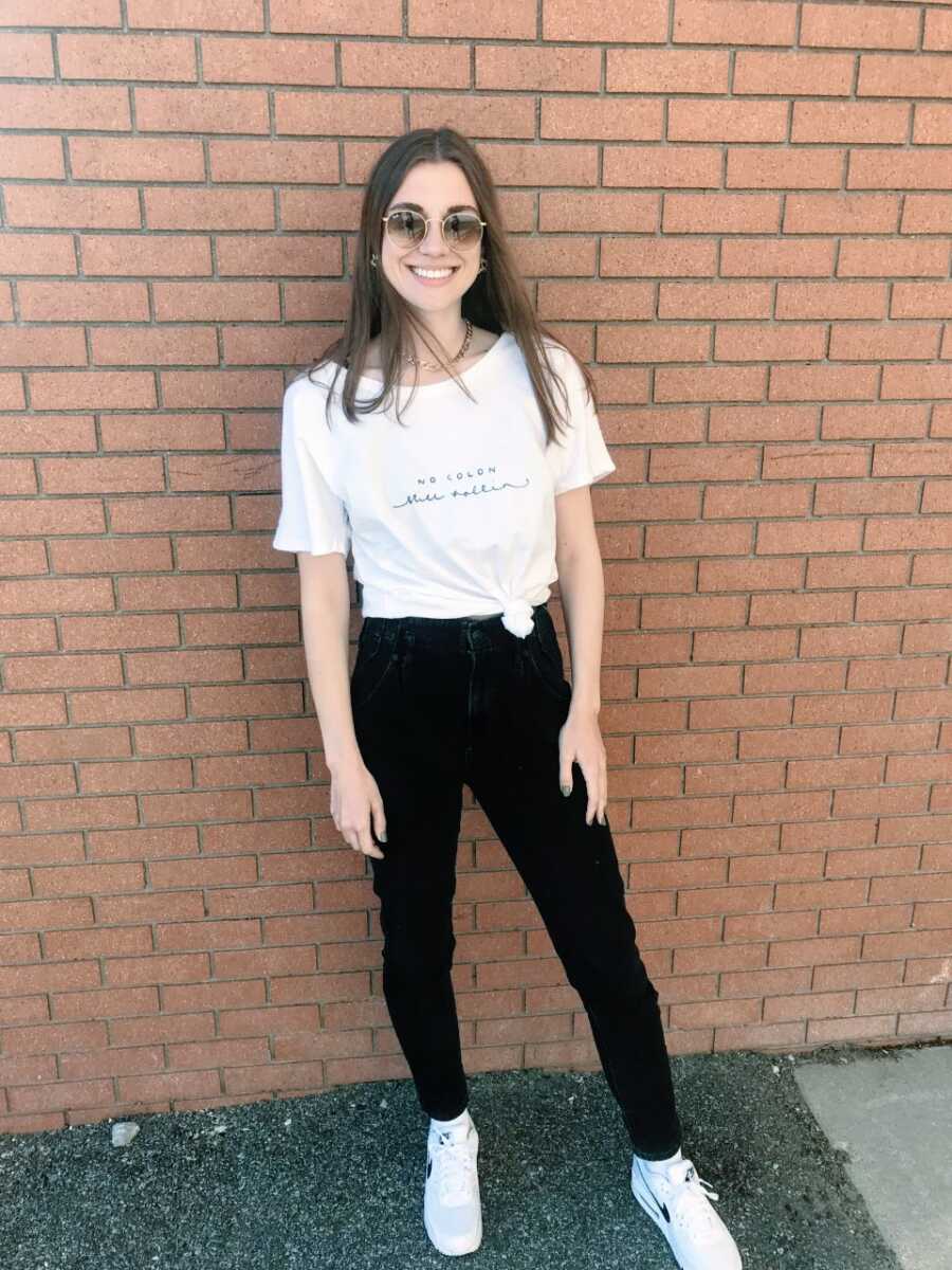 Young woman who had a colectomy due to ulcerative colitis takes a photo wearing a shirt that says "No colon, still rollin'"