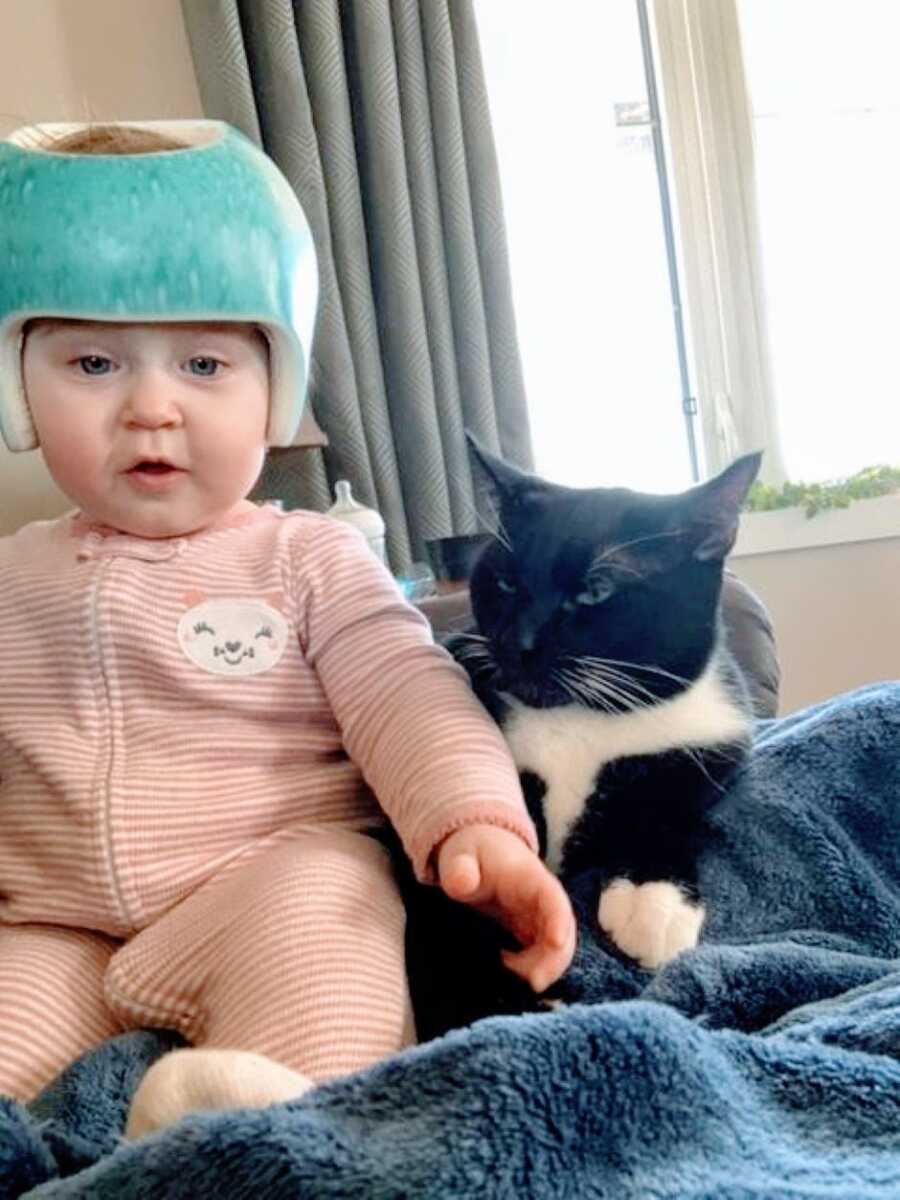 Little girl with hydrocephalus and torticollis wears a cranial helmet while sitting next to her family cat