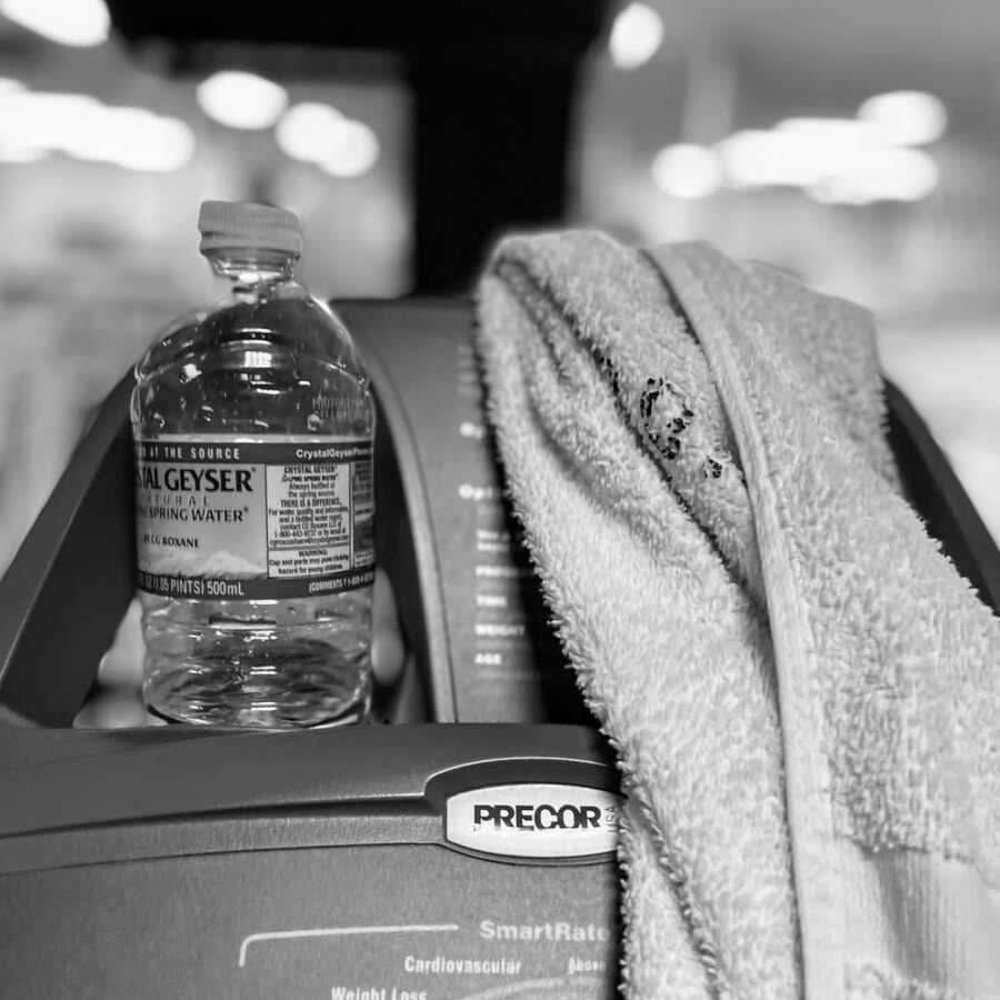 Woman snaps photo of her water bottle and sweat towel while working out at the gym