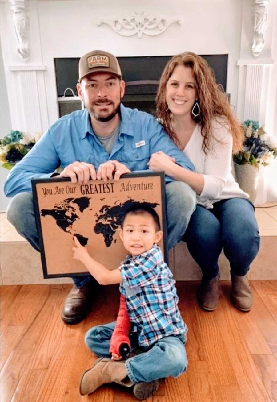 Couple pose with their adopted son and a sign that says "You are our greatest adventure"