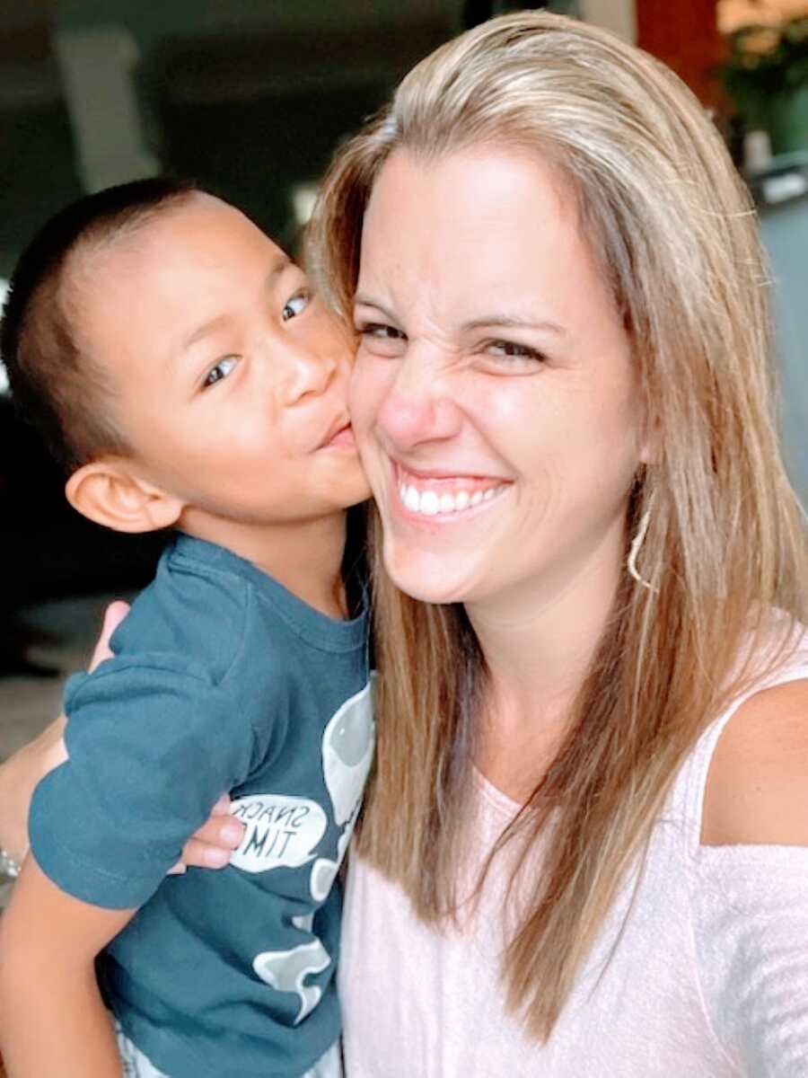 Adoptive mom smiles big while her adopted son kisses her on the cheek