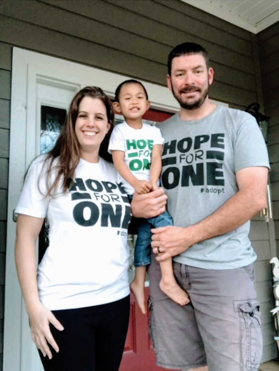 Couple pose with their adopted son all wearing matching "Hope for one #adopt" shirts as they wait to adopt another child