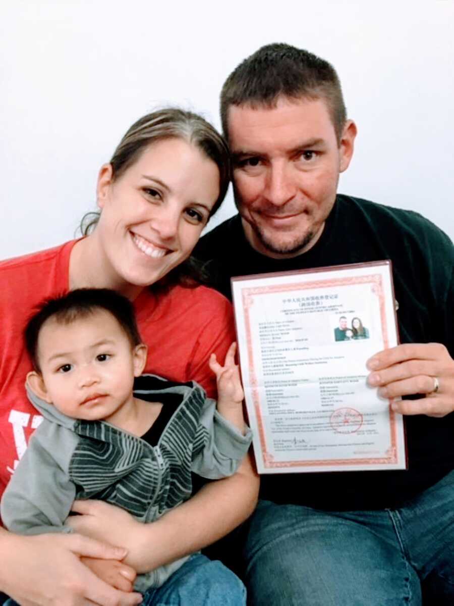 Married couple pose with their adopted son from China along with their official adoption papers