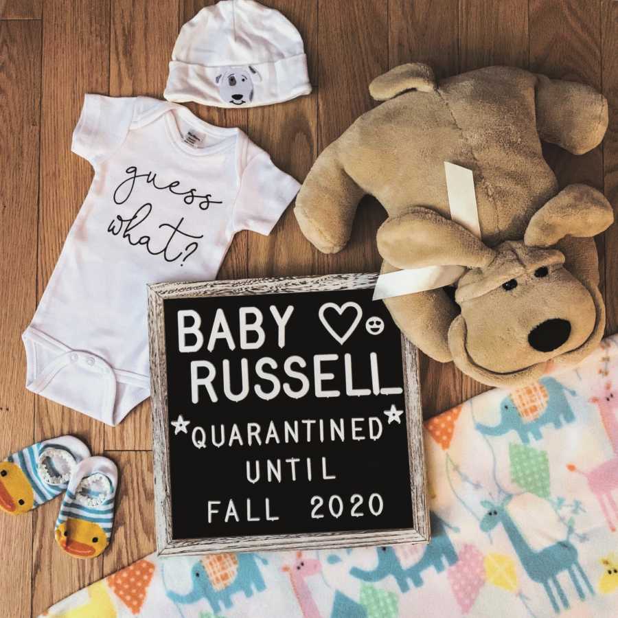 Expecting parents take pregnancy announcement photos with baby clothes and toys and a sign