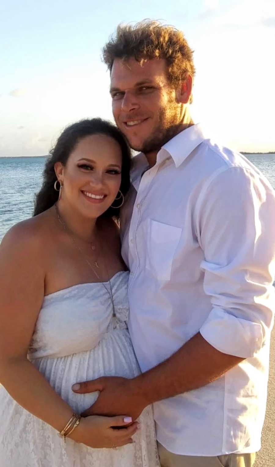 Young couple expecting their first child together smile at the camera while holding the woman's baby bump