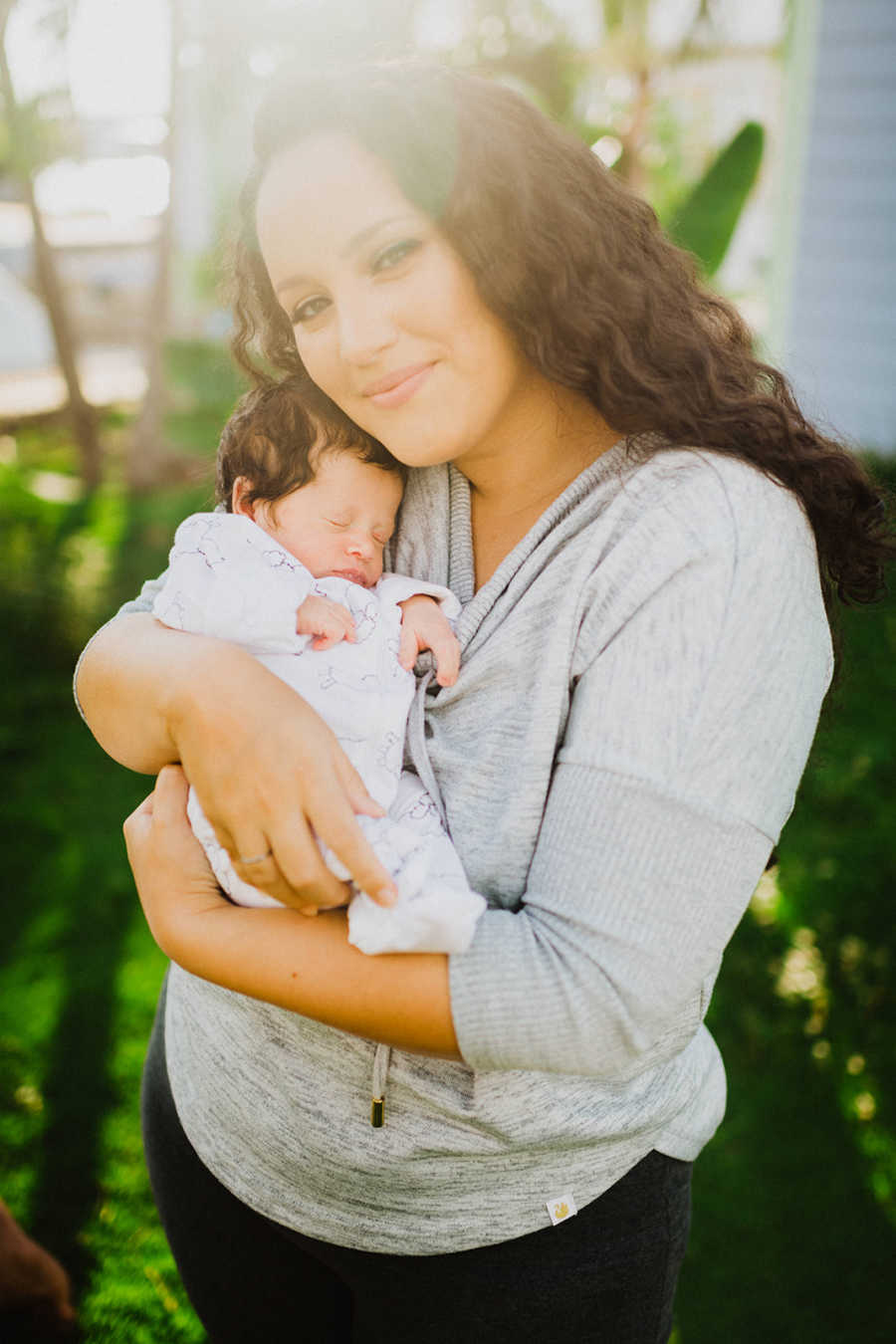 Mom holds her newborn born with a limb difference during golden hour in their backyard