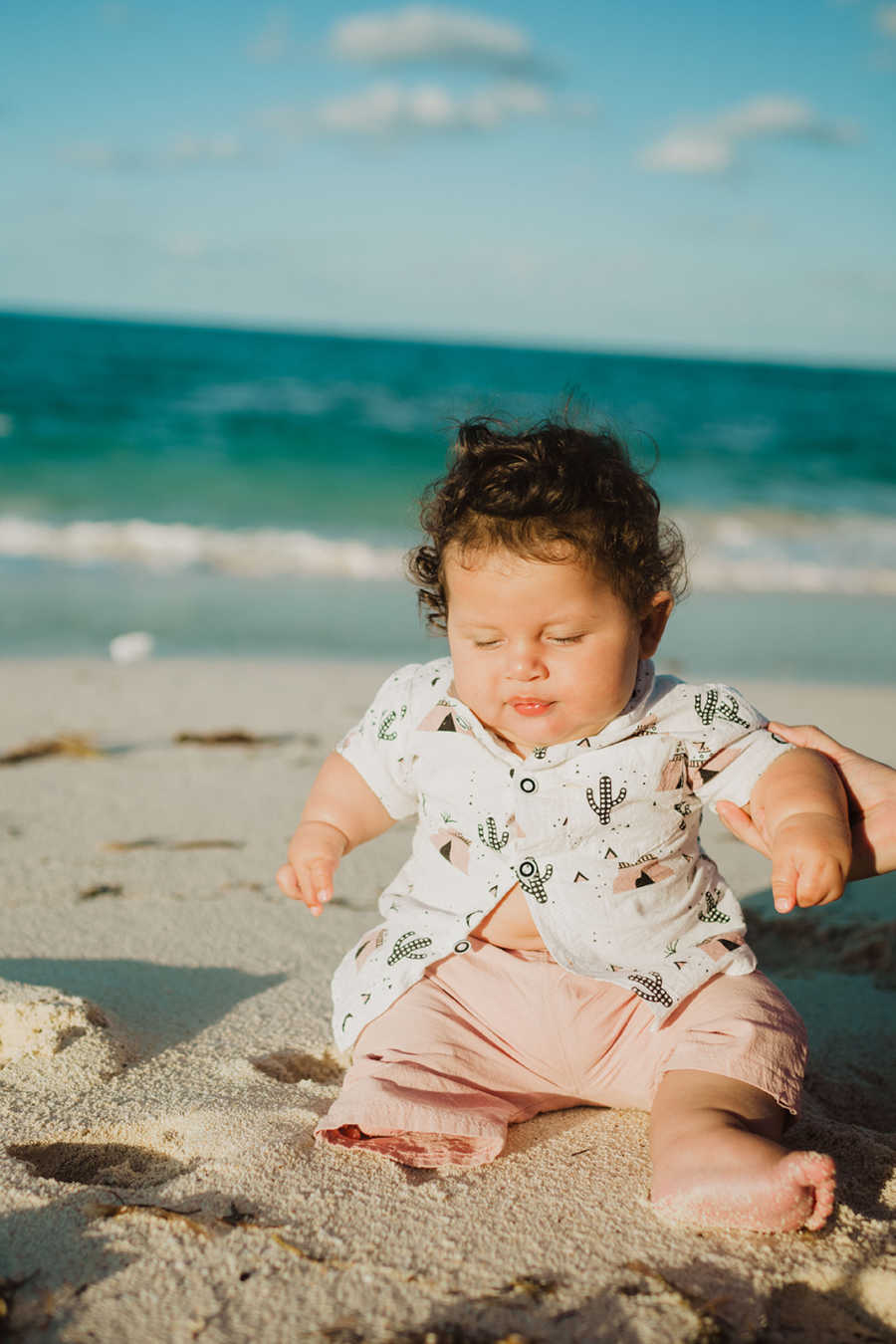 Little boy born with a limb difference sits on the beach and plays in the sand