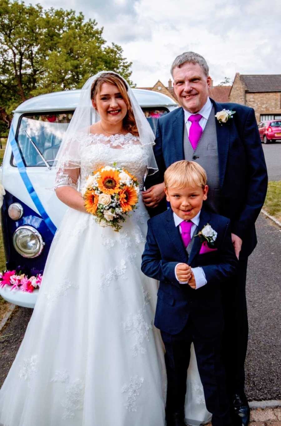 Young girl takes a photo with her dad while standing in front of a Volkswagen Bus on her wedding day