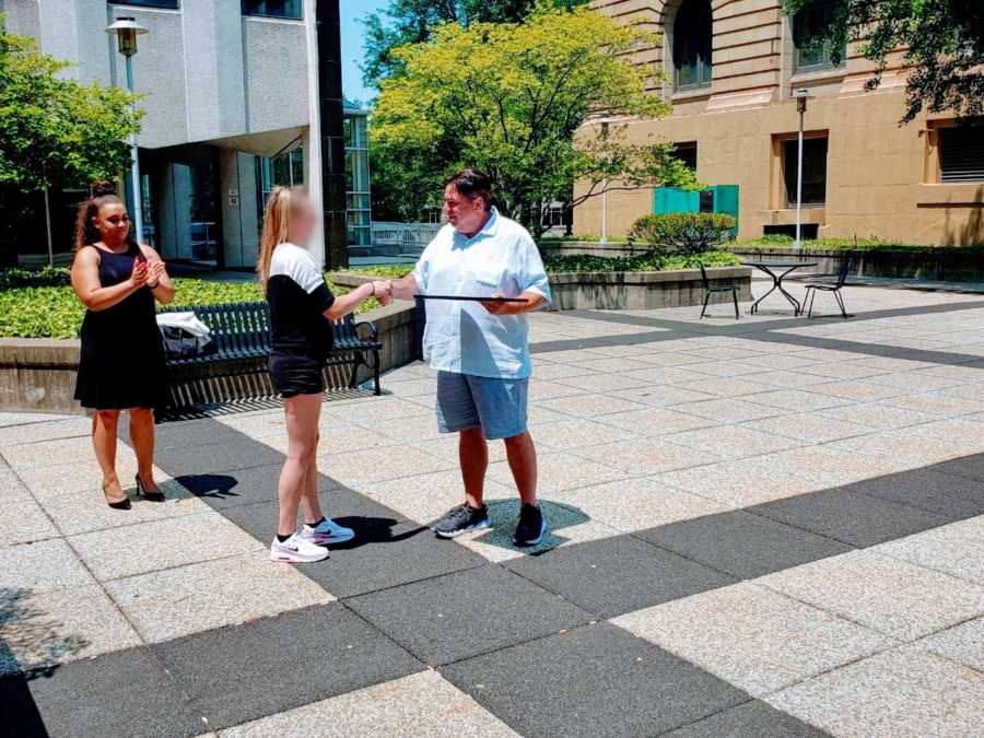 Woman graduating from recovery program shakes hands with probation officer while receiving a certificate