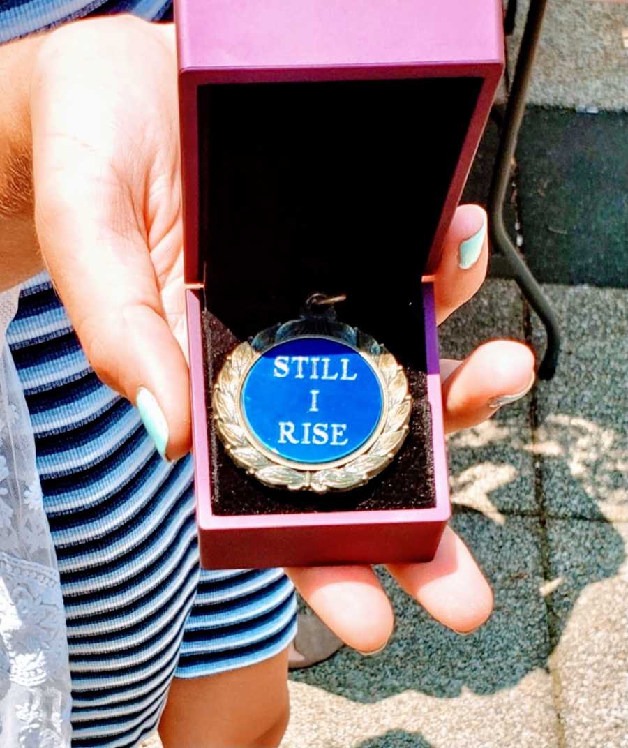 Woman graduating from program that helped her overcome human trafficking takes photo of medal that says "Still I Rise"