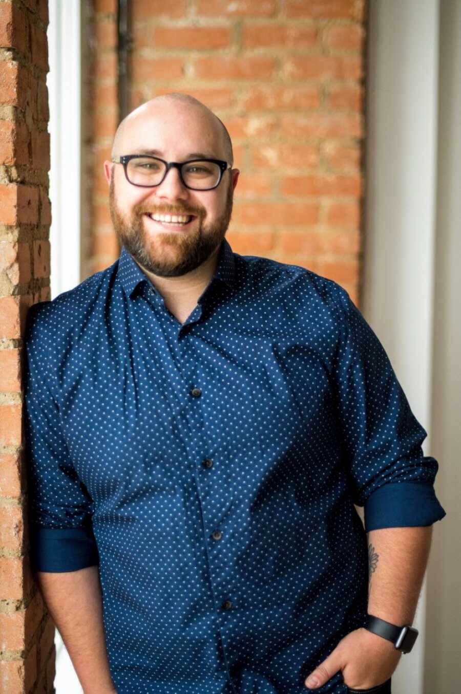 Young man who overcame a suicide attempt smiles for a headshot in a polka dot button down shirt