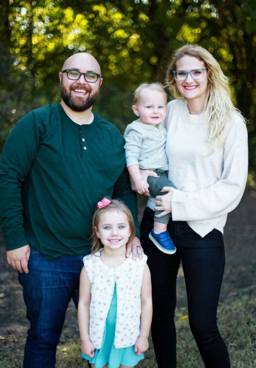 Young man advocating for mental health and suicide prevention smiles big in a family photo with his wife and two kids