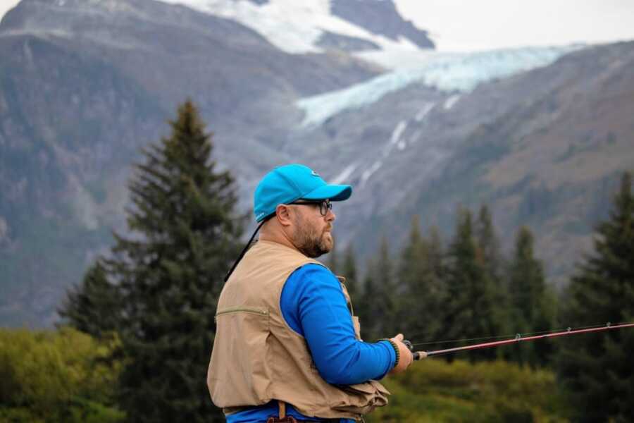 Young man of faith working through mental health struggles takes a serious photo while fishing in a mountainous area