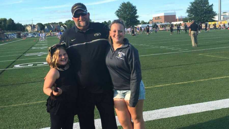 Football coach with his two daughters on football field