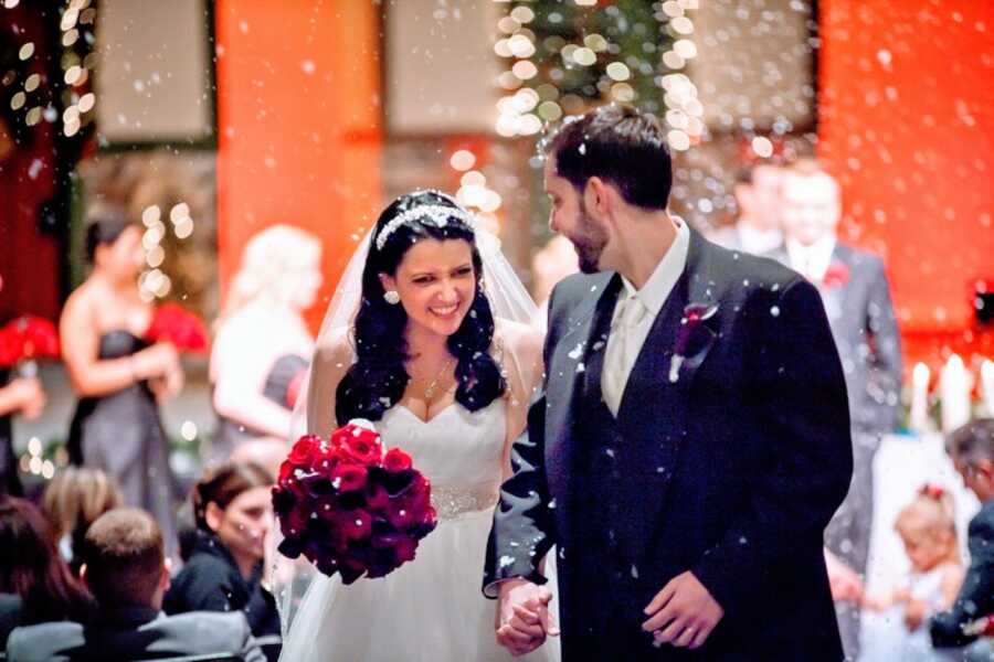 Newlywed couple smile big as they walk down the aisle together with fake snow coming down