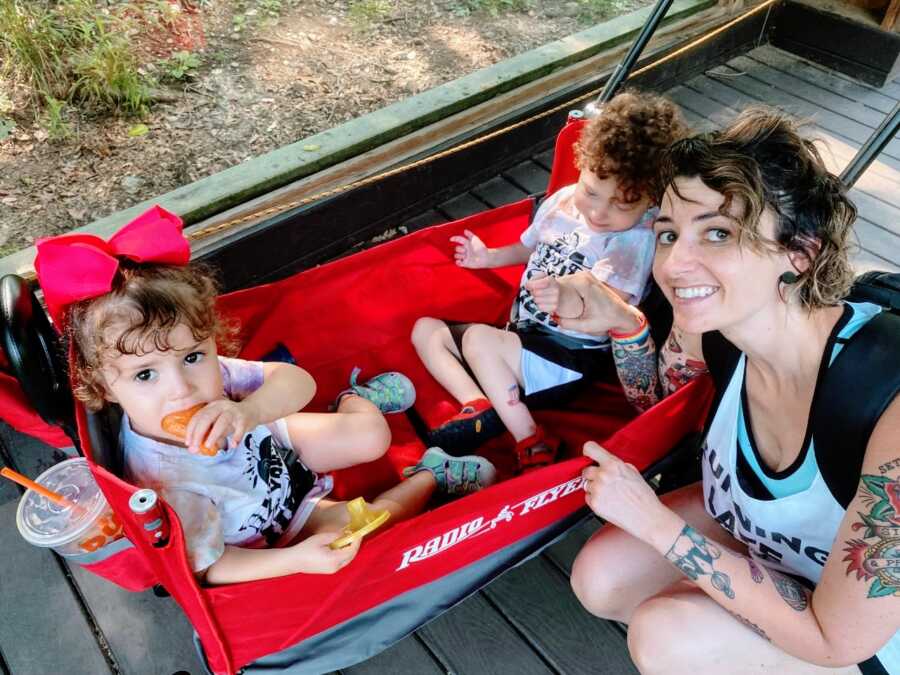 Solo mom takes a photo with her two kids in a red Radio Flyer wagon while at the zoo