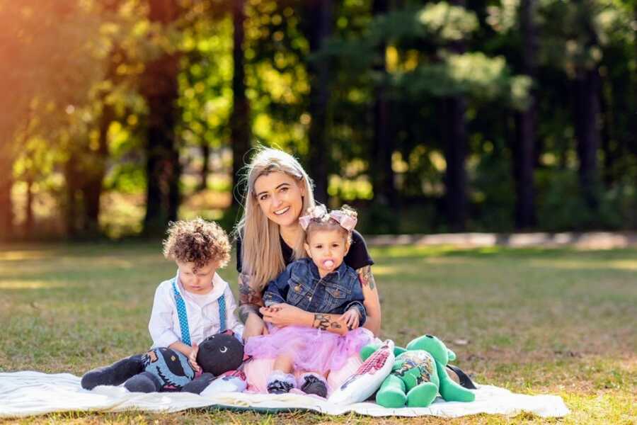 Young widow sits on a blanket with her two children after losing her husband to covid