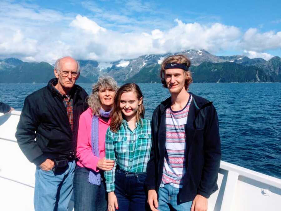 Young girl in green plaid shirt poses with her family on a boat with a mountain scene behind them