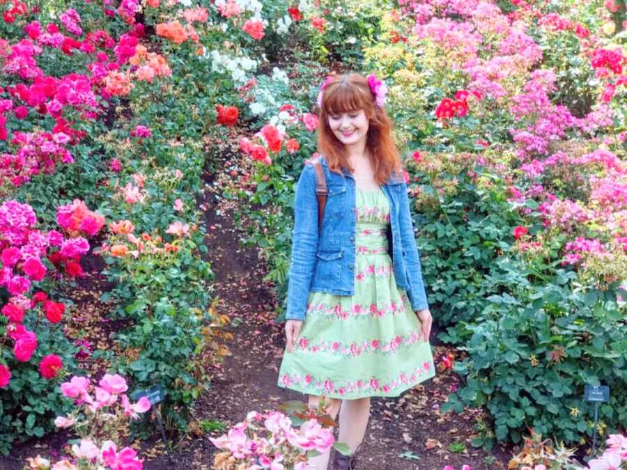 Young woman accepting her autistic identity poses in front of a ton of flowers in a floral dress with matching flowers in her hair