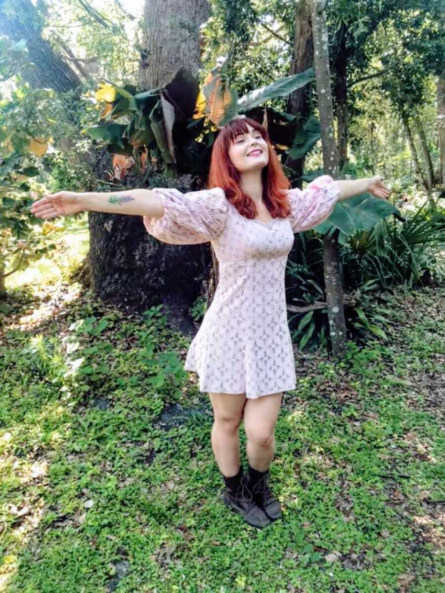 Young woman embraces her autistic identity and the nature around her while on a walk in boots and a dress