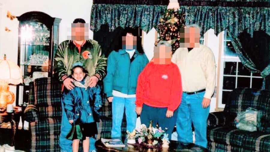 Young girl experiencing sexual abuse from her father poses with her family in front of the Christmas tree with a green dress on