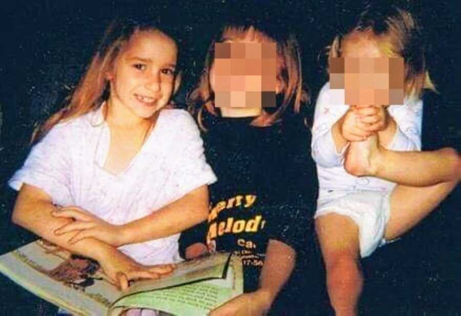 Young girl sits with her two sisters while she reads them a bedtime story