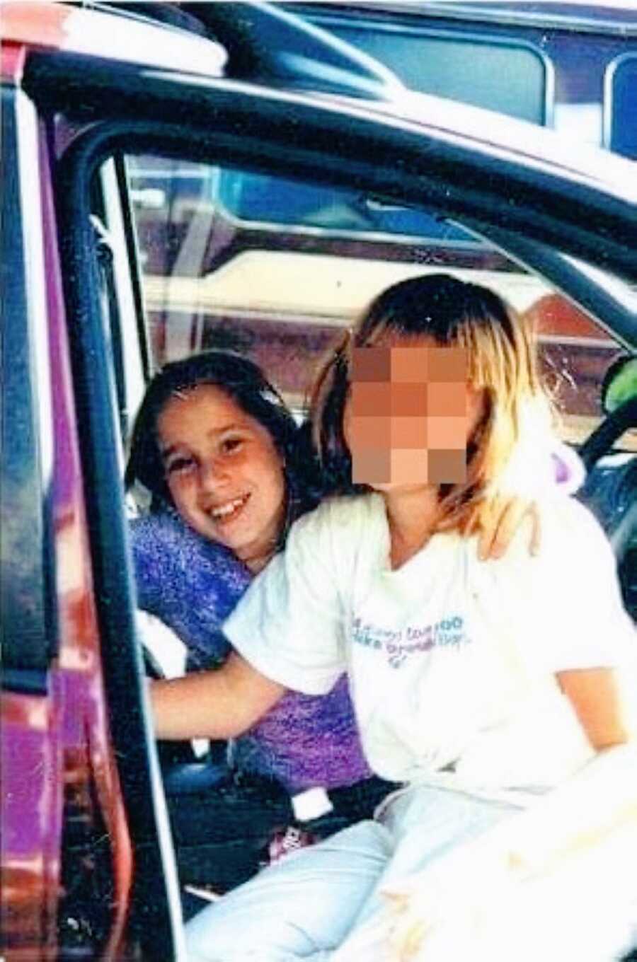 Little girl and her sister sit in a car together while smiling and spending time together