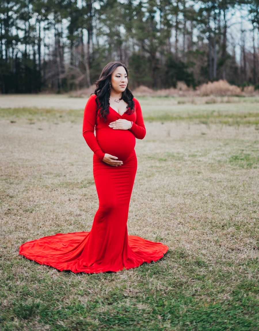 maternity photo of woman in a red dress with her hands on her stomach