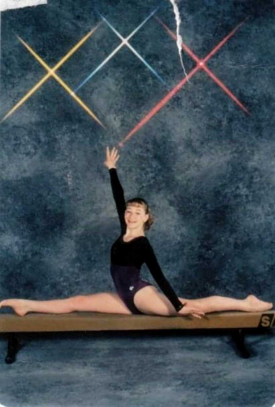 Young gymnast poses on a beam in a long-sleeved leotard