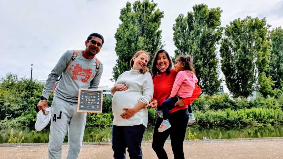 Family of three take photos with their surrogate as she carries their triplet boys