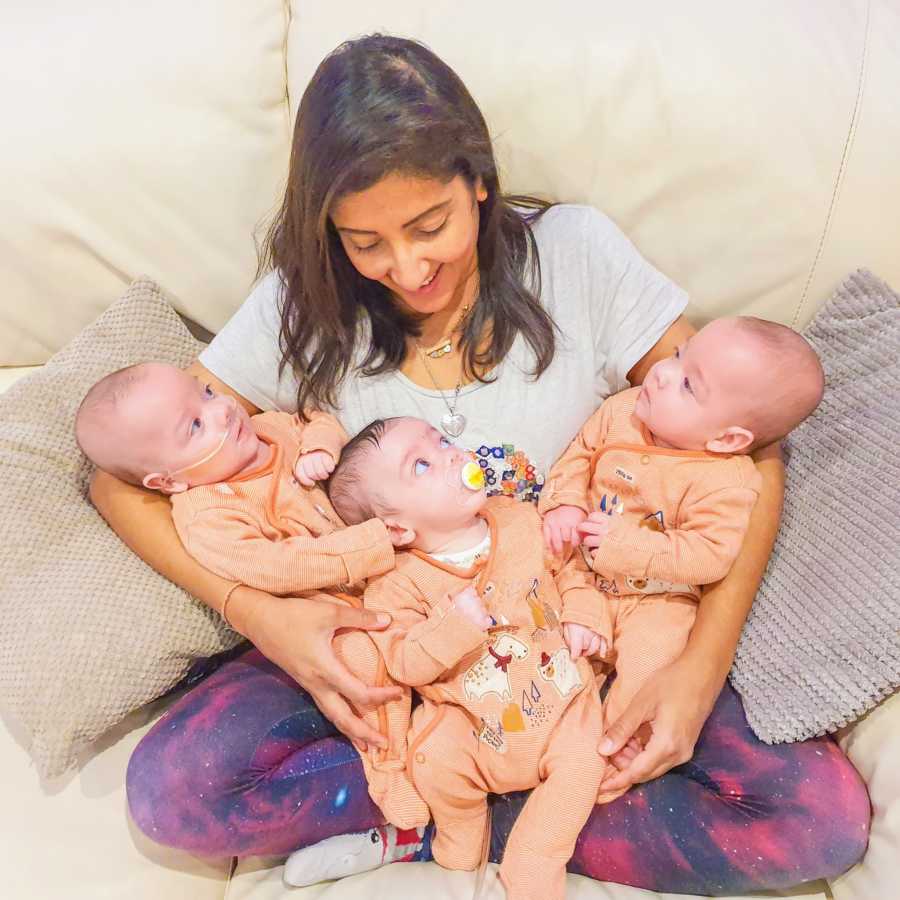 Mom of four holds her newborn triplets while they all stare up at her with their big blue eyes