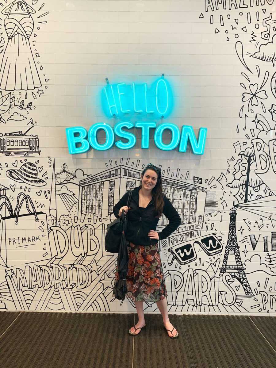 woman in front of a 'hello Boston' wall
